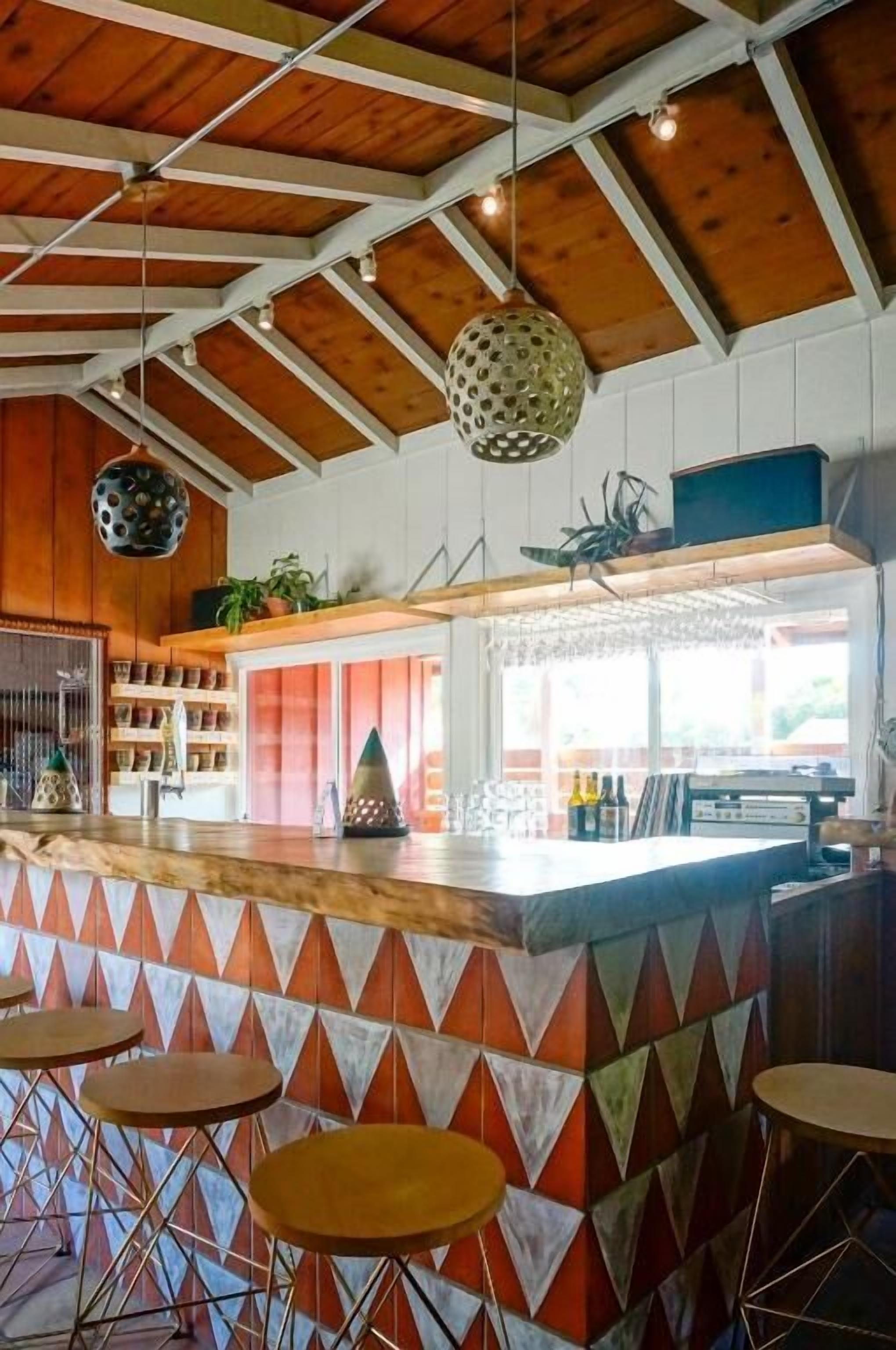 A bar area with a wooden ceiling, geometric patterned wall, and bar stools.