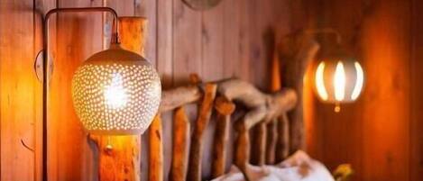A wooden cabin interior with a bed, a wall-mounted lamp, and a small cactus on a nightstand.