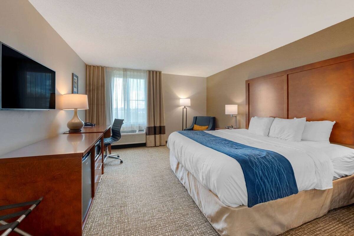 Una habitación de hotel con cama, escritorio, silla, lámparas y televisor.