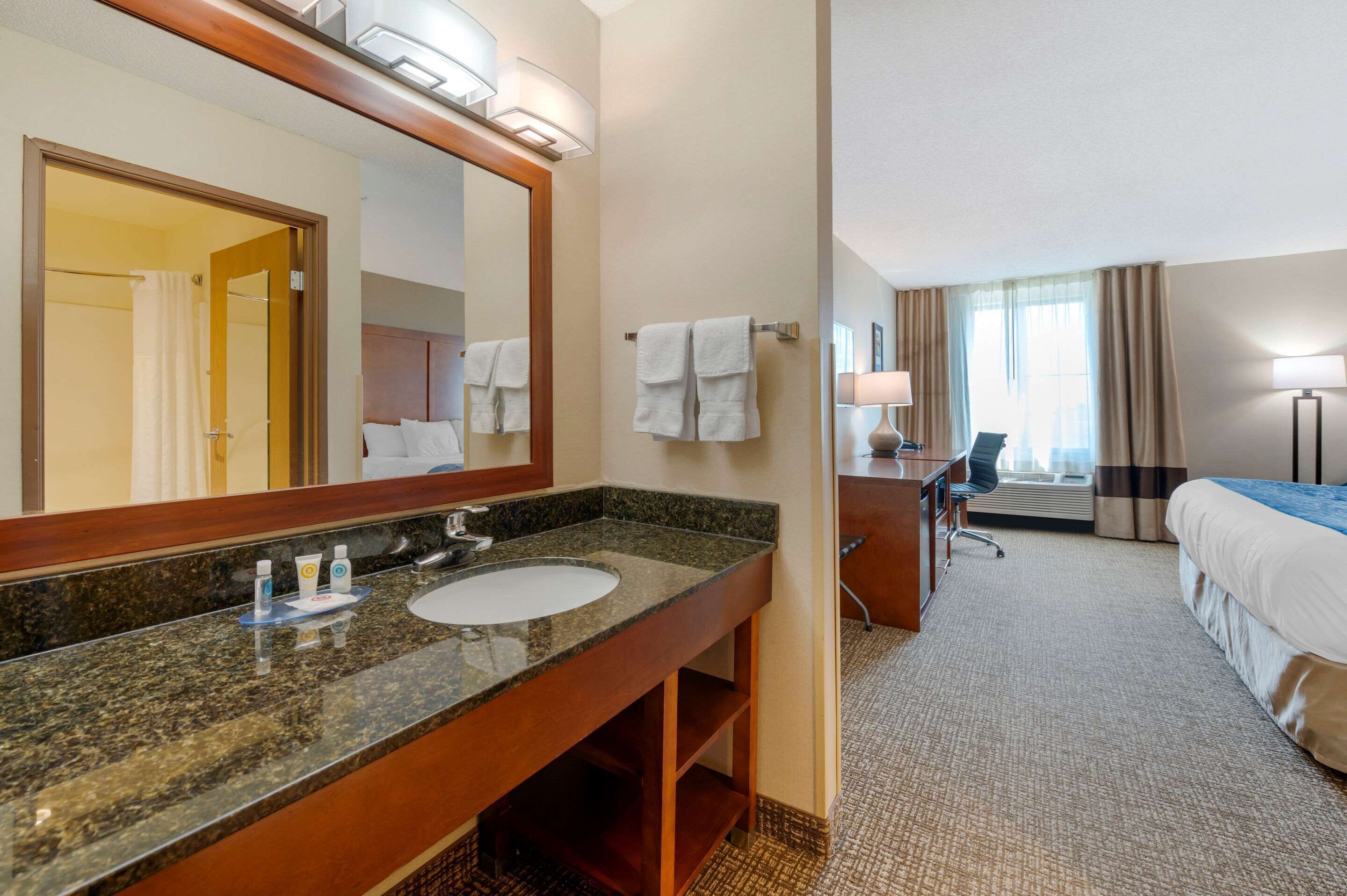A hotel bathroom with a granite sink, a large mirror, and a shower area.
