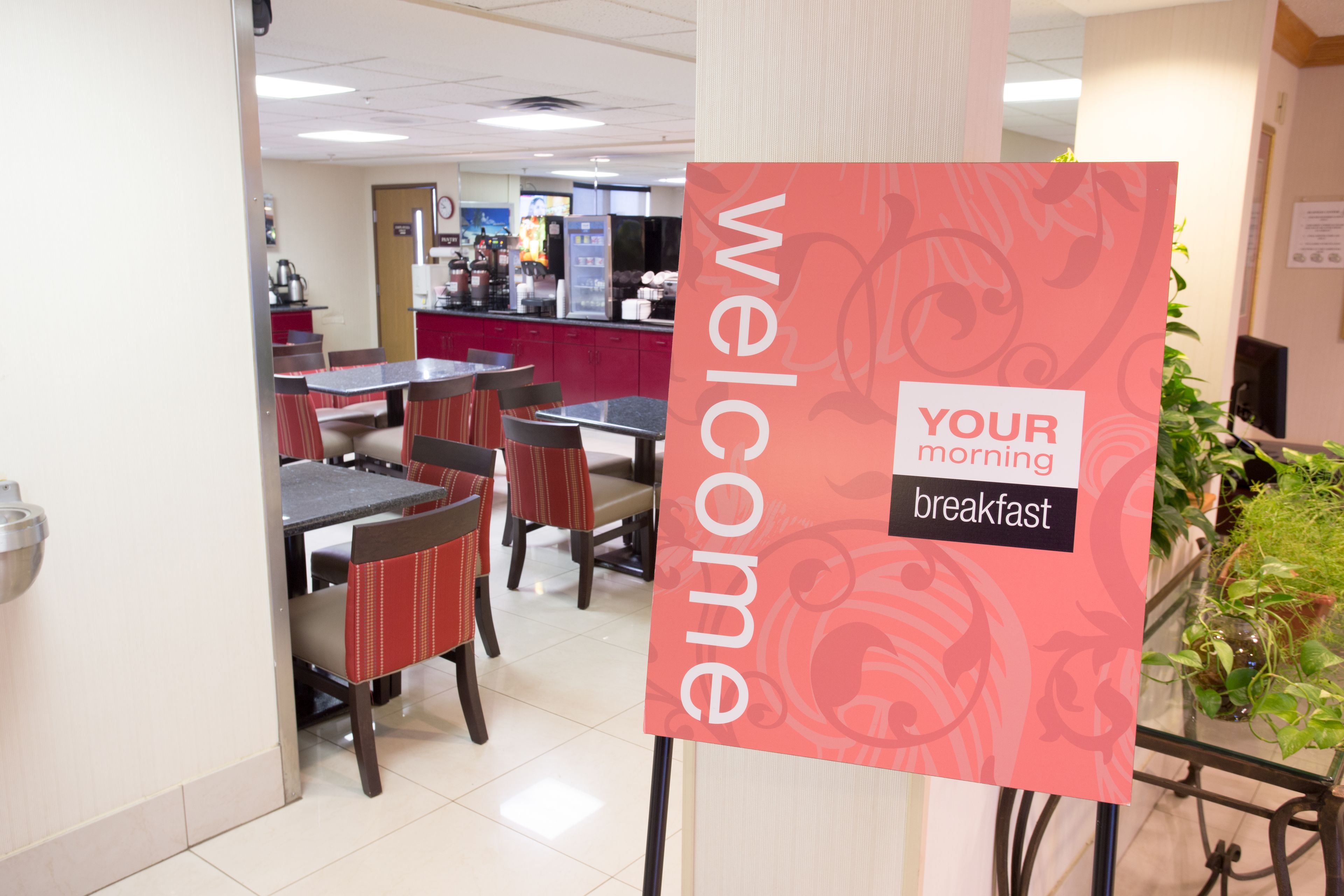 A breakfast area with tables and chairs, a sign reading "WELCOME YOUR morning breakfast", and a counter with food items.
