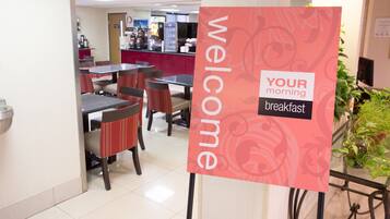 A breakfast area with tables and chairs, a sign reading "WELCOME YOUR morning breakfast", and a counter with food items.