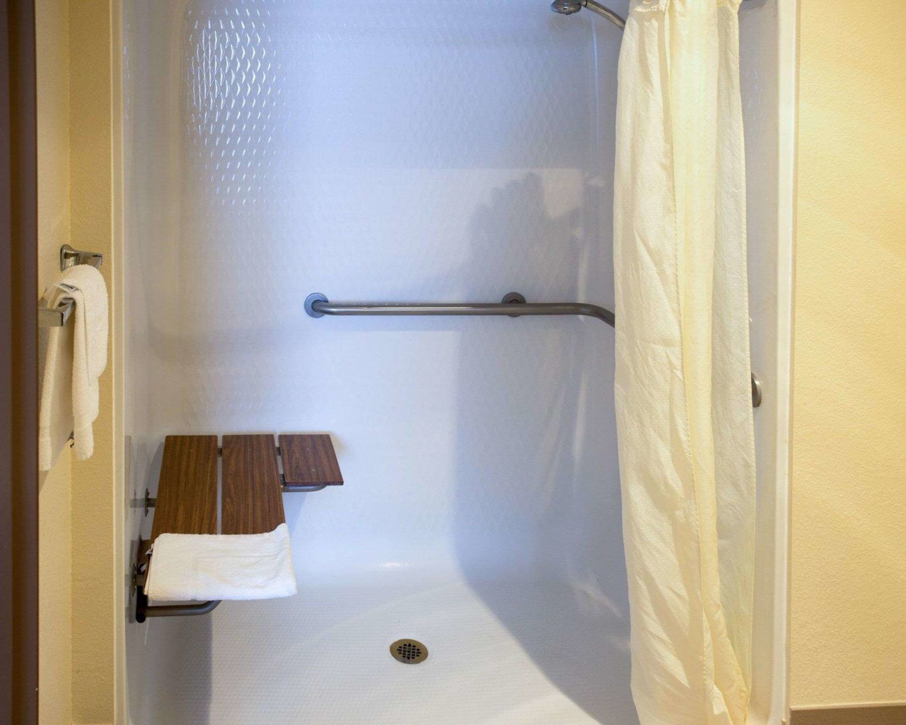 A shower stall with a grab bar, a towel rack, and a wooden bench.
