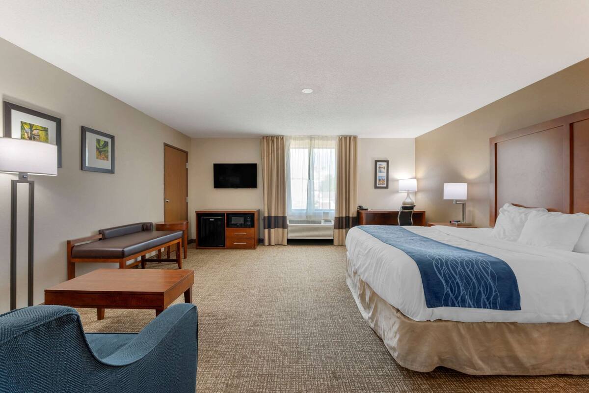 Habitación de hotel con cama, escritorio, silla, televisor y ventana con cortinas.