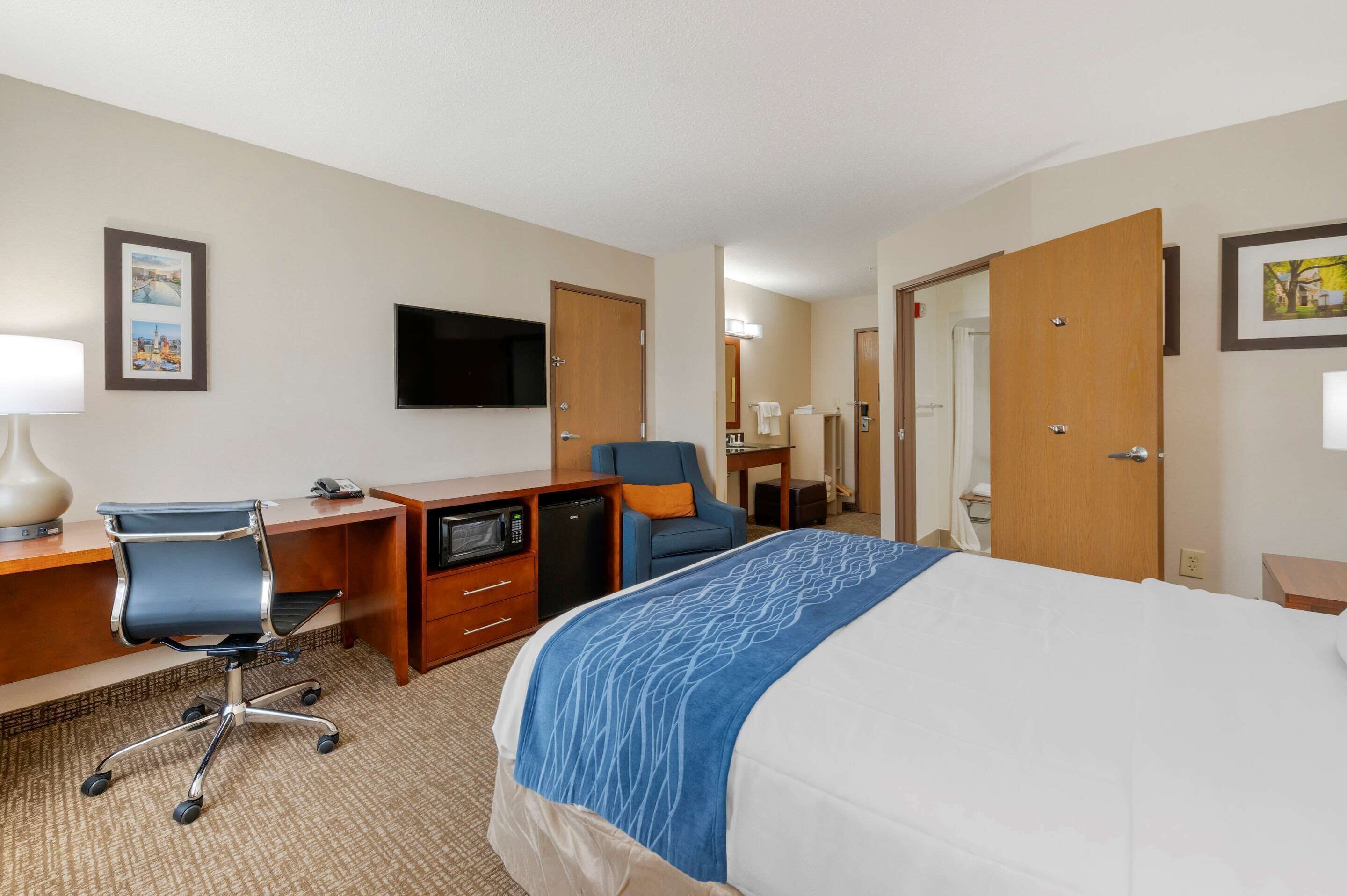 Een hotelkamer met een bed, bureau, stoel, televisie en een magnetron.