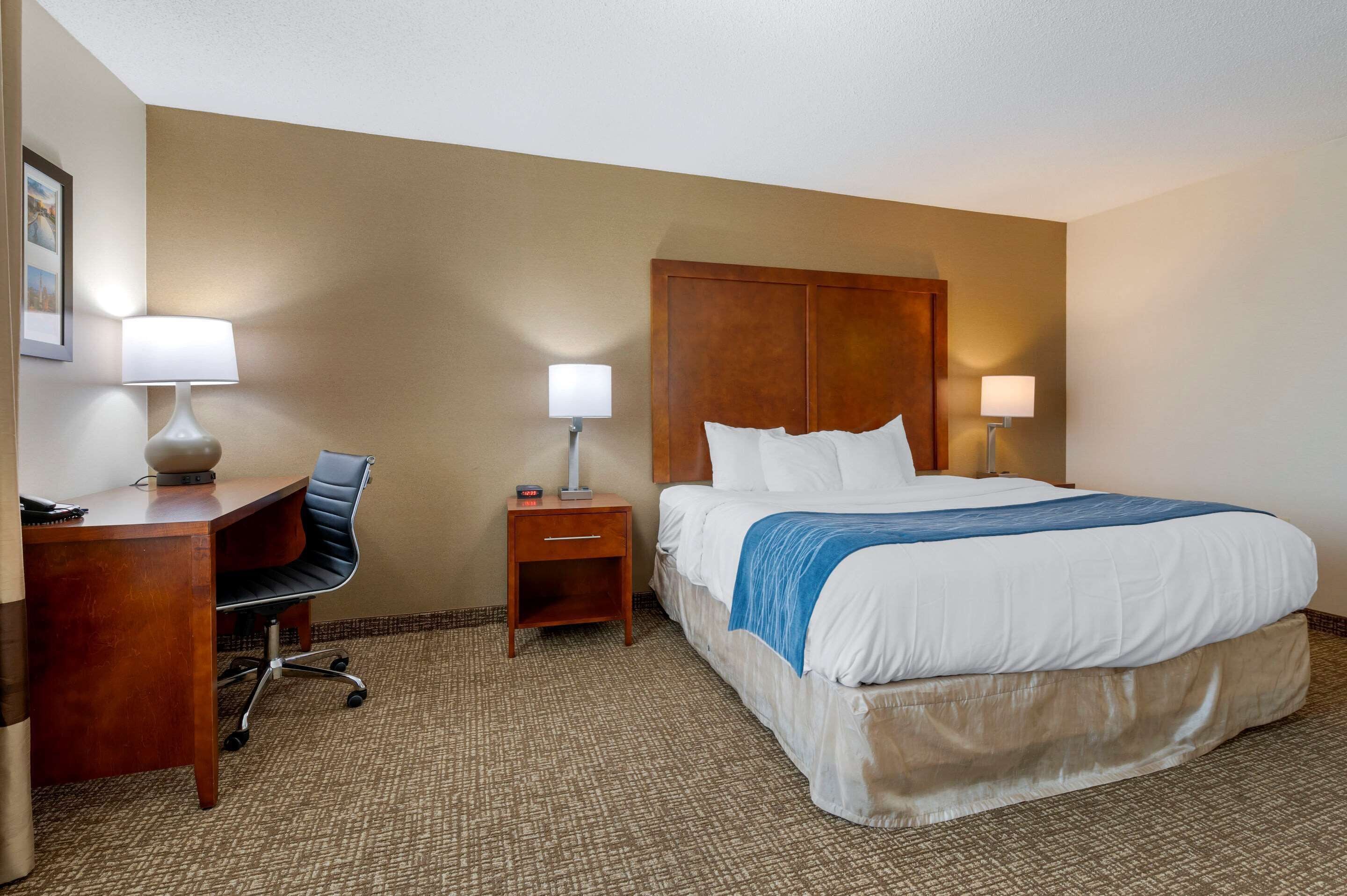 A hotel room with a bed, desk, chair, and two bedside lamps.
