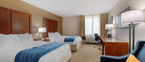 A hotel room with two beds, a desk, a chair, and a TV.