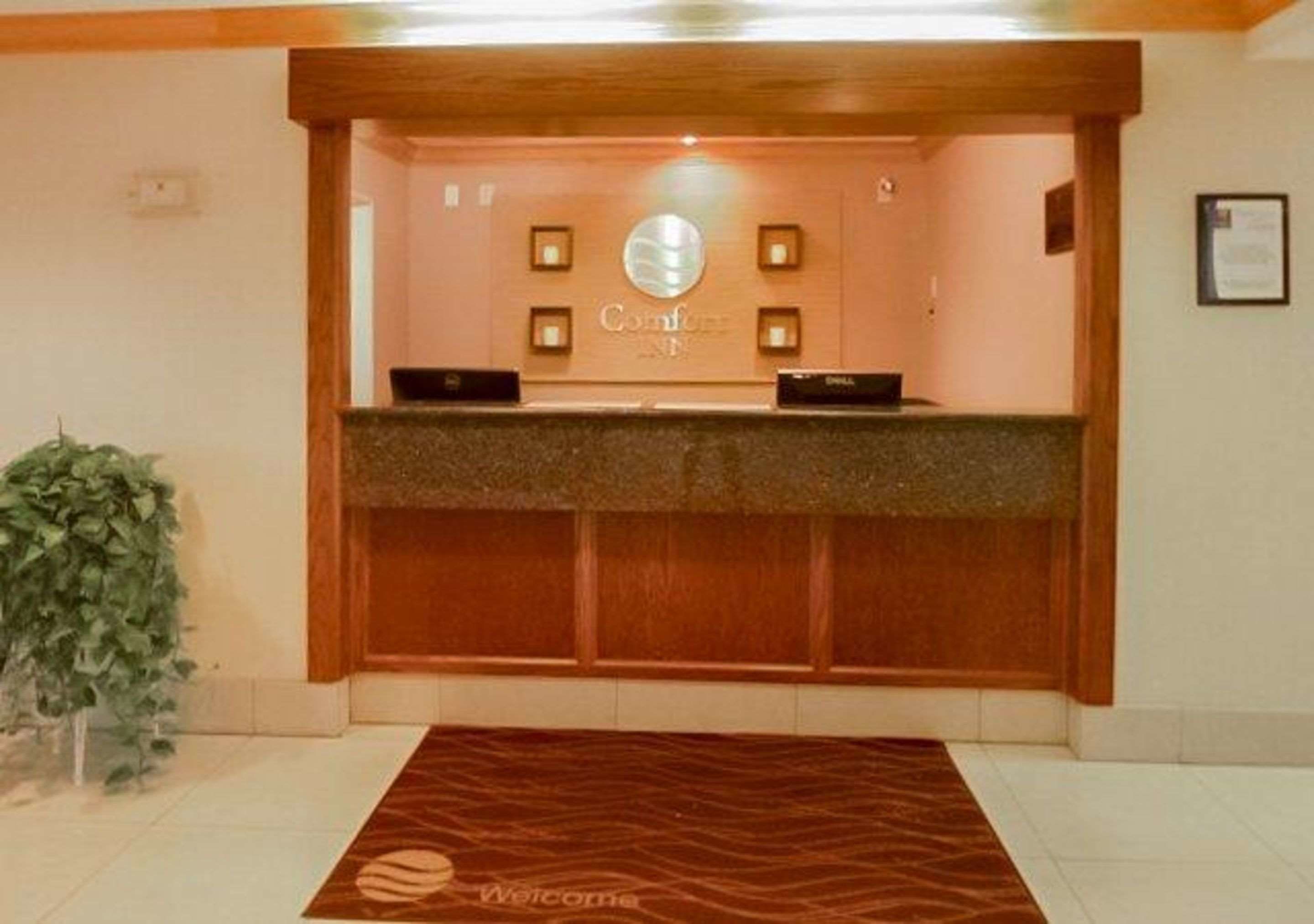 A reception desk with a wooden counter, a sign above it, and a framed certificate on the wall.