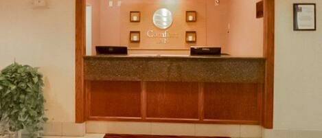 A reception desk with a wooden counter, a sign above it, and a framed certificate on the wall.