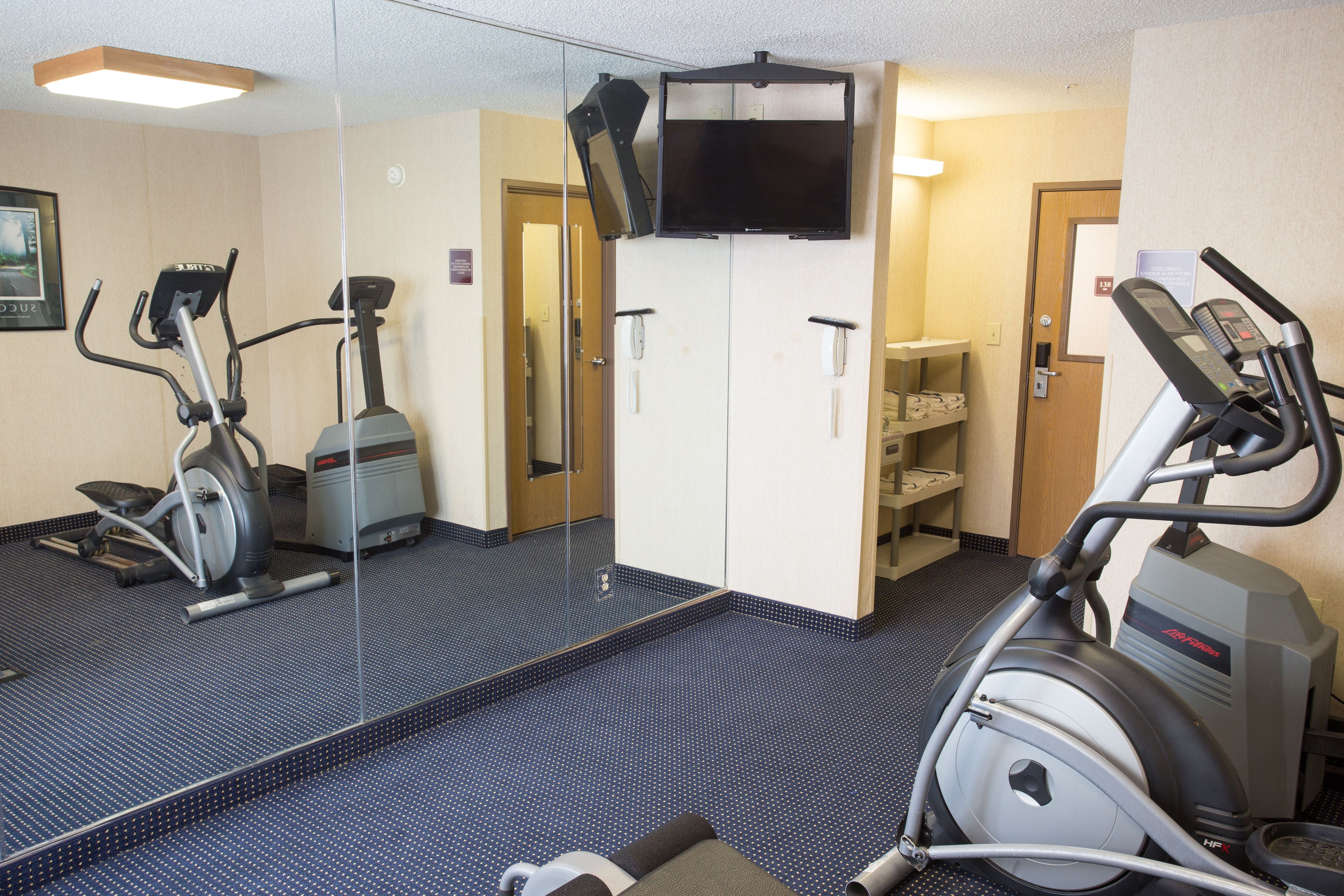 A hotel room with a mirrored wall, exercise equipment, a television, and a door leading to a bathroom.