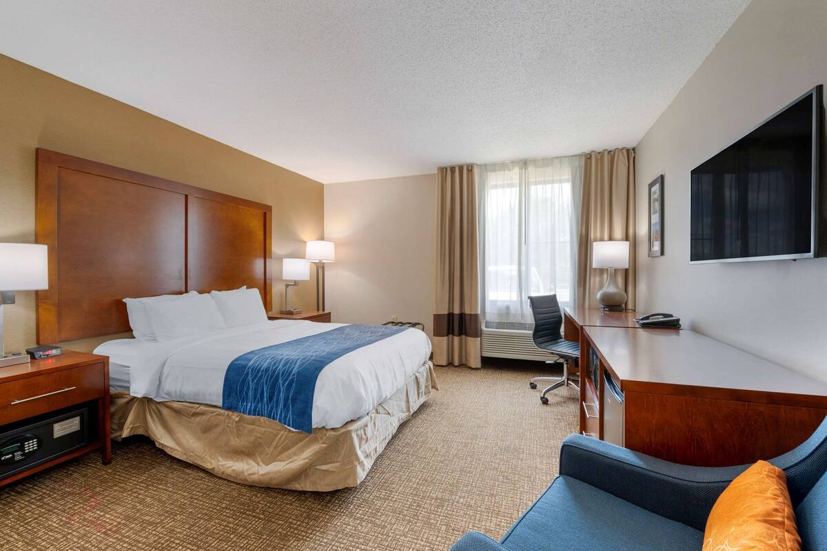 Habitación de hotel con cama, escritorio, silla, televisor y ventana con cortinas.