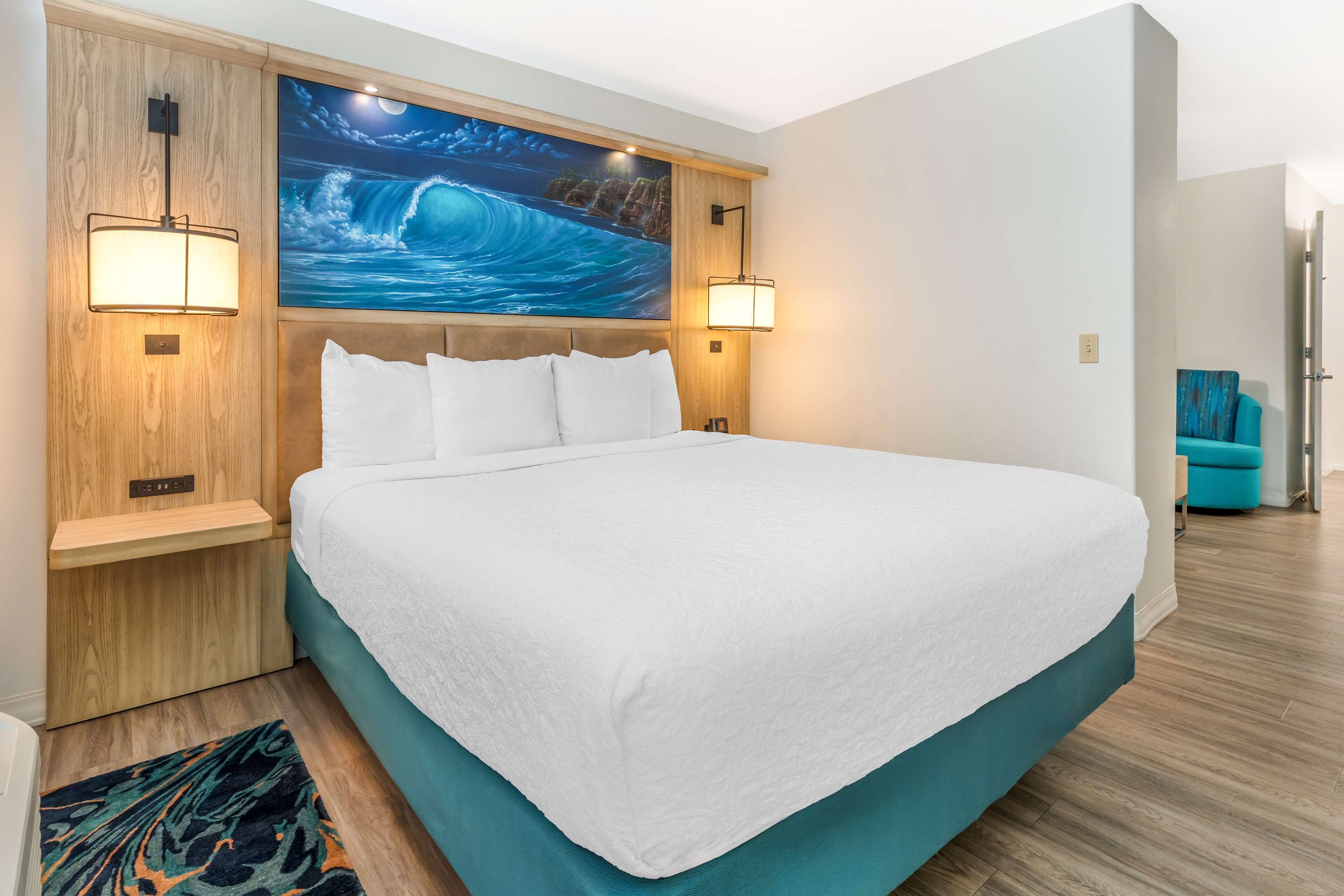 Una cama grande con ropa blanca, cabecera de madera y dos lámparas fijadas a la pared.