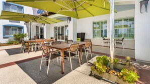 An outdoor patio with a wooden table and chairs, green umbrellas, and potted plants. - Best Western Plus Capitola By-the-sea Inn & Suites (Santa Cruz)
