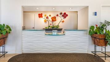 Un área de recepción con un diseño de pared ondulada, un mostrador con cubierta de vidrio y dos plantas en macetas.
