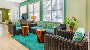 A spacious living area with wicker furniture, a teal carpet, and large windows with blinds. - Best Western Plus Capitola By-the-sea Inn & Suites (Santa Cruz)