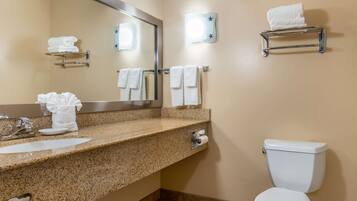 A bathroom with a granite countertop, a sink, a mirror, a toilet, and towel racks.