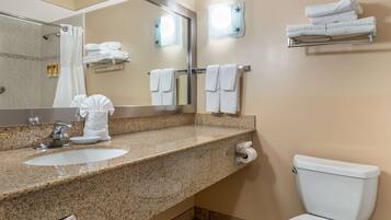 A bathroom with a granite countertop sink, a mirror, a toilet, and towel racks.