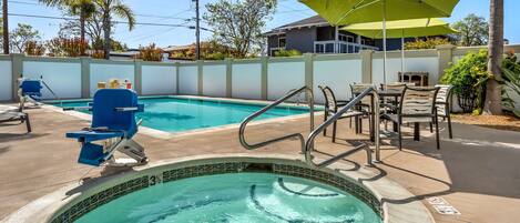 A swimming pool with a hot tub, lounge chairs, and a table with umbrellas.
