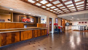A reception area with a wooden reception desk, a digital screen, and a view of the kitchen area. - Best Western Plus Brandywine Inn & Suites (Monticello)