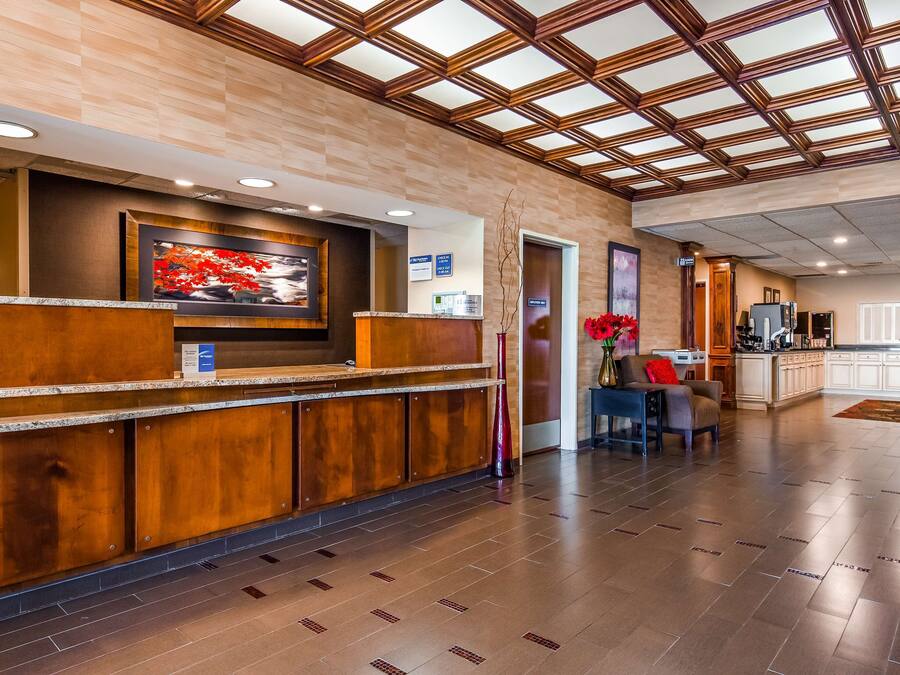 A reception area with a wooden reception desk, a digital screen, and a view of the kitchen area.