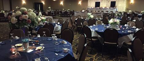 Un salón de banquetes con mesas redondas dispuestas para cenar, con manteles azules y centros de mesa blancos.