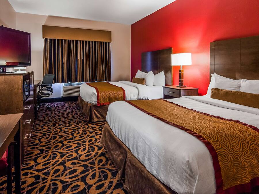 A hotel room with two beds, a desk, a television, and a red accent wall.