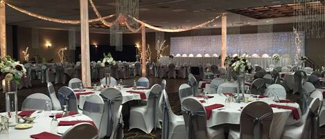 Un salón de banquetes con mesas redondas, sillas grises y manteles blancos.