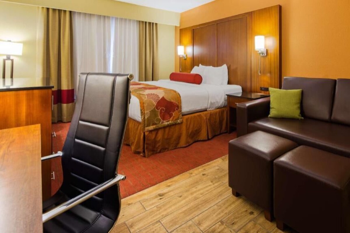 A hotel room with a bed, a desk, a chair, a sofa, and a small table.