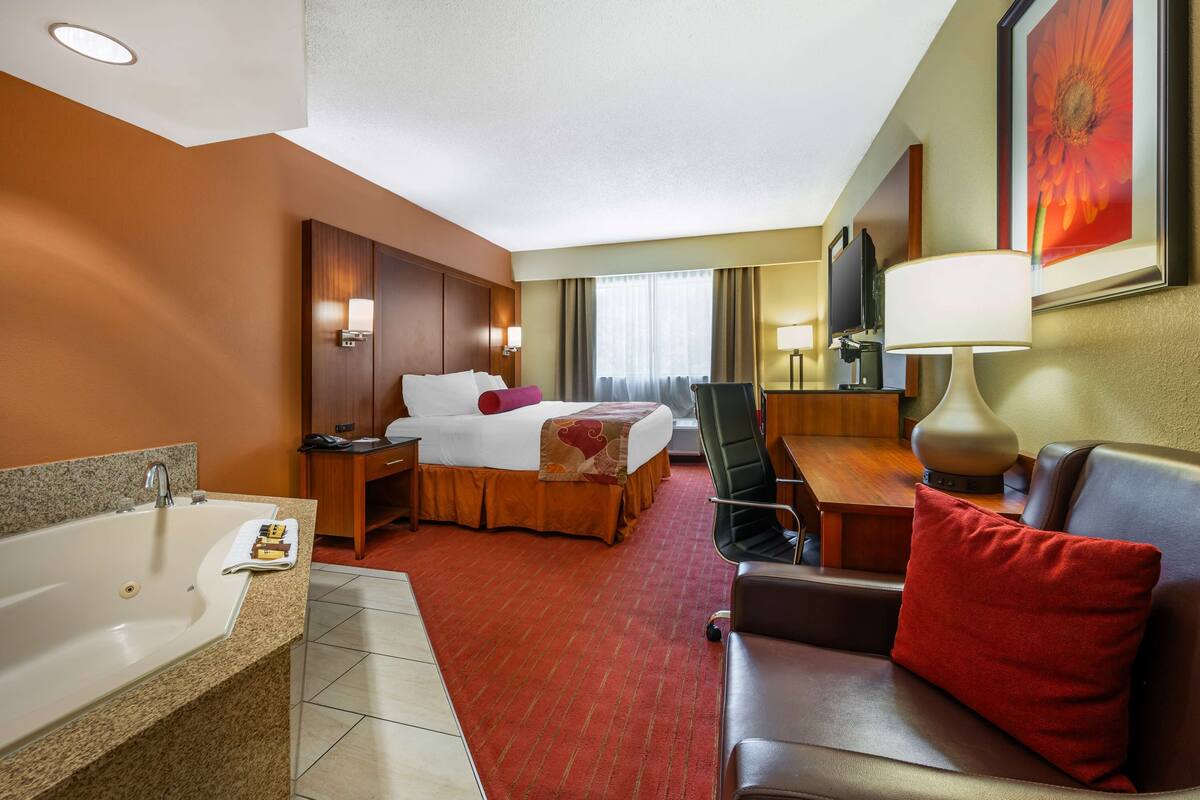 Habitación de hotel con cama, escritorio, silla, lámpara, televisión y baño con bañera y lavamanos.