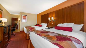 A hotel room with two beds, a desk, and a chair. There are two wall-mounted lamps and a framed picture on the wall.