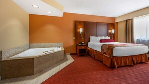 A hotel room with a large bathtub, a bed with a red pillow, and a nightstand with a lamp. - Best Western Plus Georgetown Corporate Center Hotel (Georgetown)