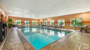 An indoor swimming pool with clear blue water, surrounded by lounge chairs and tables, with large windows offering views of greenery outside. - Best Western Plus Georgetown Corporate Center Hotel (Georgetown)
