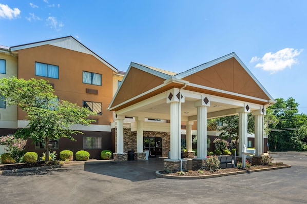 Entrada de hotel con zona de espera cubierta, columnas y estacionamiento.