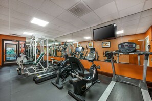 Un gimnasio con diferentes equipos de ejercicio, una cinta de correr y un espejo grande.