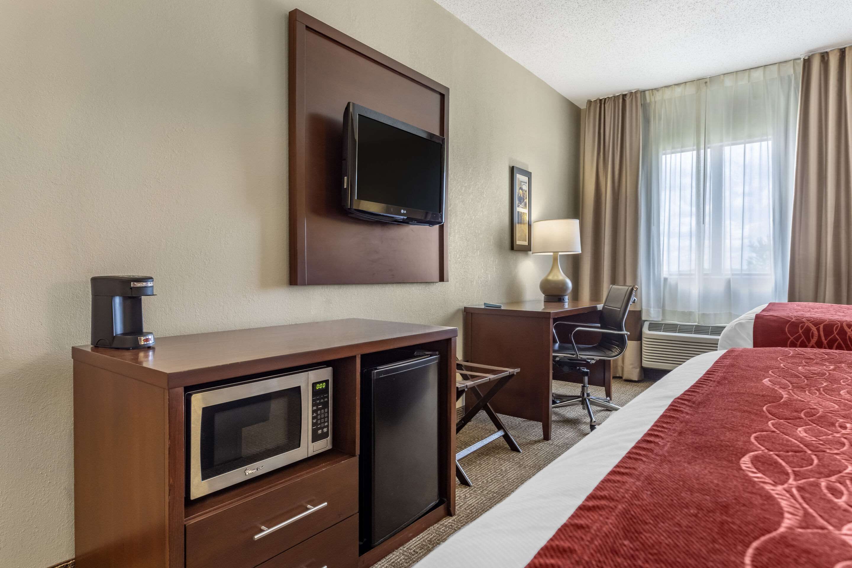 A hotel room with a bed, a desk with a computer, a TV, a coffee maker, a microwave, and a refrigerator.