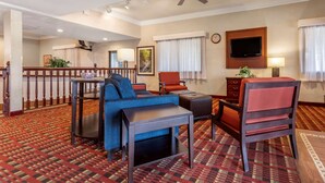 A hotel room with a blue sofa, a wooden coffee table, a red armchair, a TV mounted on the wall, and a patterned carpet. - Comfort Inn & Suites Streetsboro - Kent (Streetsboro)