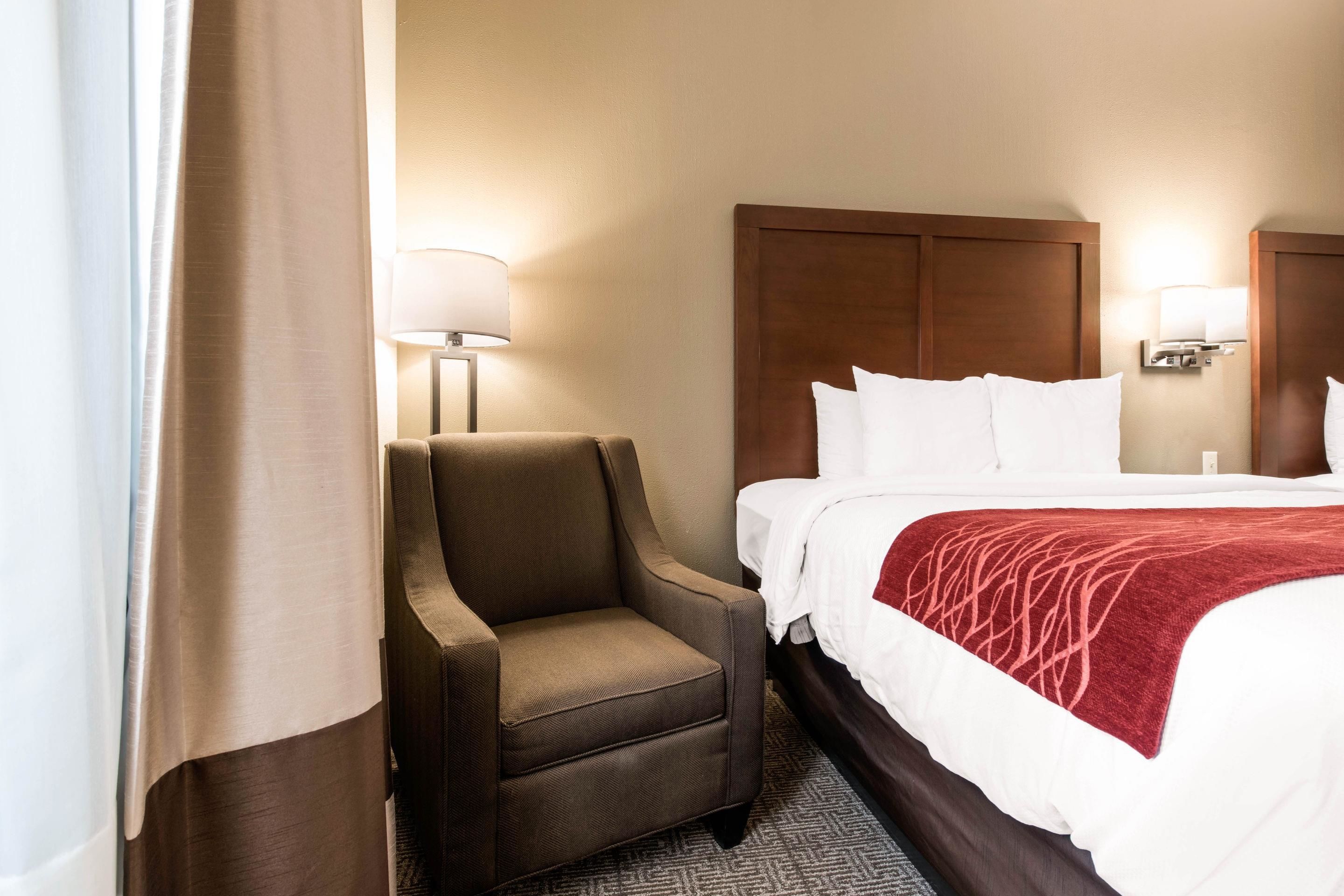 Una habitación de hotel con una cama, una silla y dos lámparas fijadas a la pared.