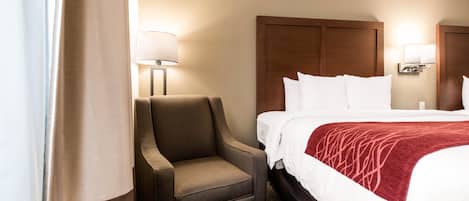 A hotel room with a bed, a chair, and two wall-mounted lamps.