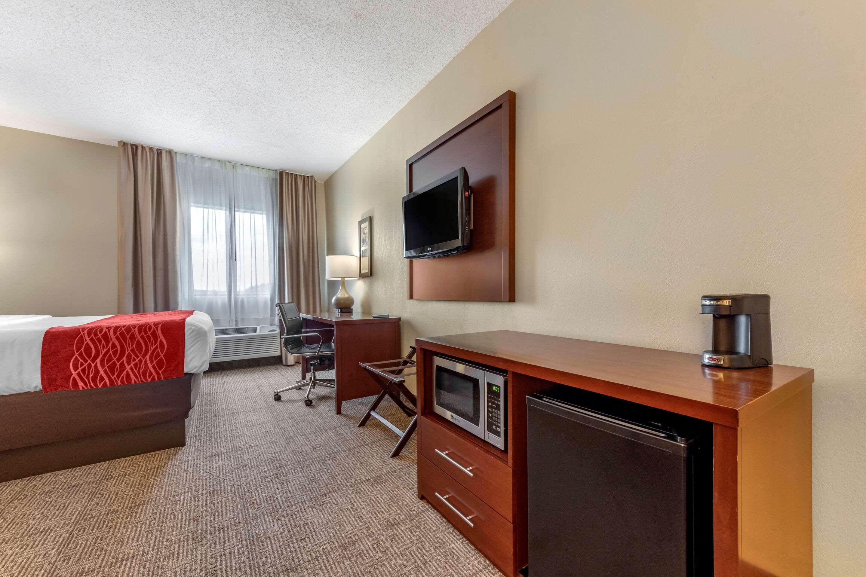 Een hotelkamer met een bed, een bureau, een magnetron, een koelkast, een televisie en een koffiezetapparaat.