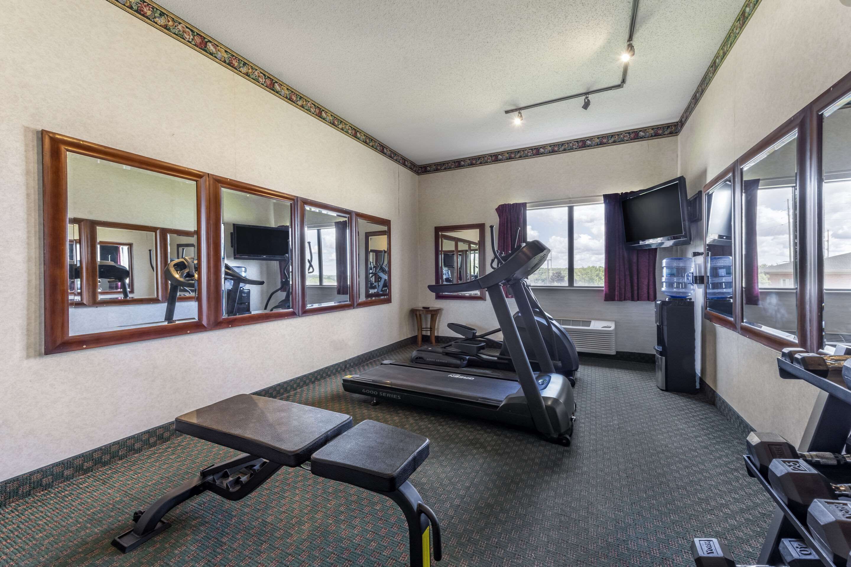 Een fitnessruimte met trainingsapparatuur, spiegels, een televisie en grote ramen.