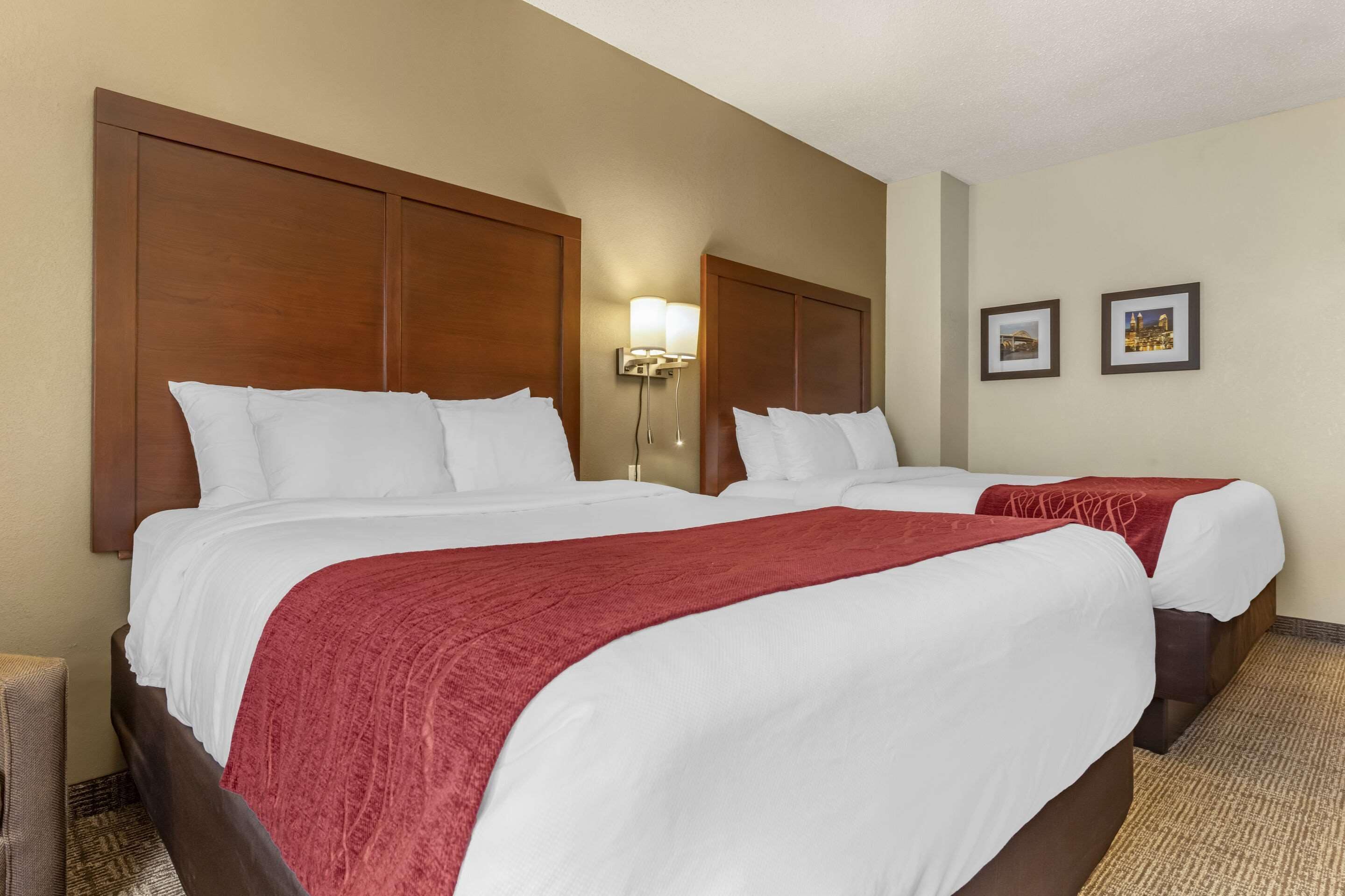 Ein Hotelzimmer mit zwei Betten, einem Holz-Kopfteil, einer Wandlampe und zwei gerahmten Bildern.