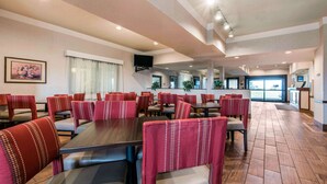 A spacious dining area with multiple tables and chairs, a television mounted on the wall, and a view of the kitchen area in the background. - Comfort Inn & Suites Streetsboro - Kent (Streetsboro)