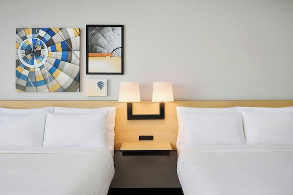 Quarto de hotel com duas camas, uma mesa de cabeceira com abajures e duas obras de arte emolduradas na parede.
