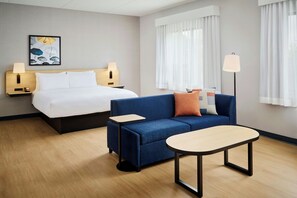 A hotel room with a bed, a sofa, a small table, and a lamp.