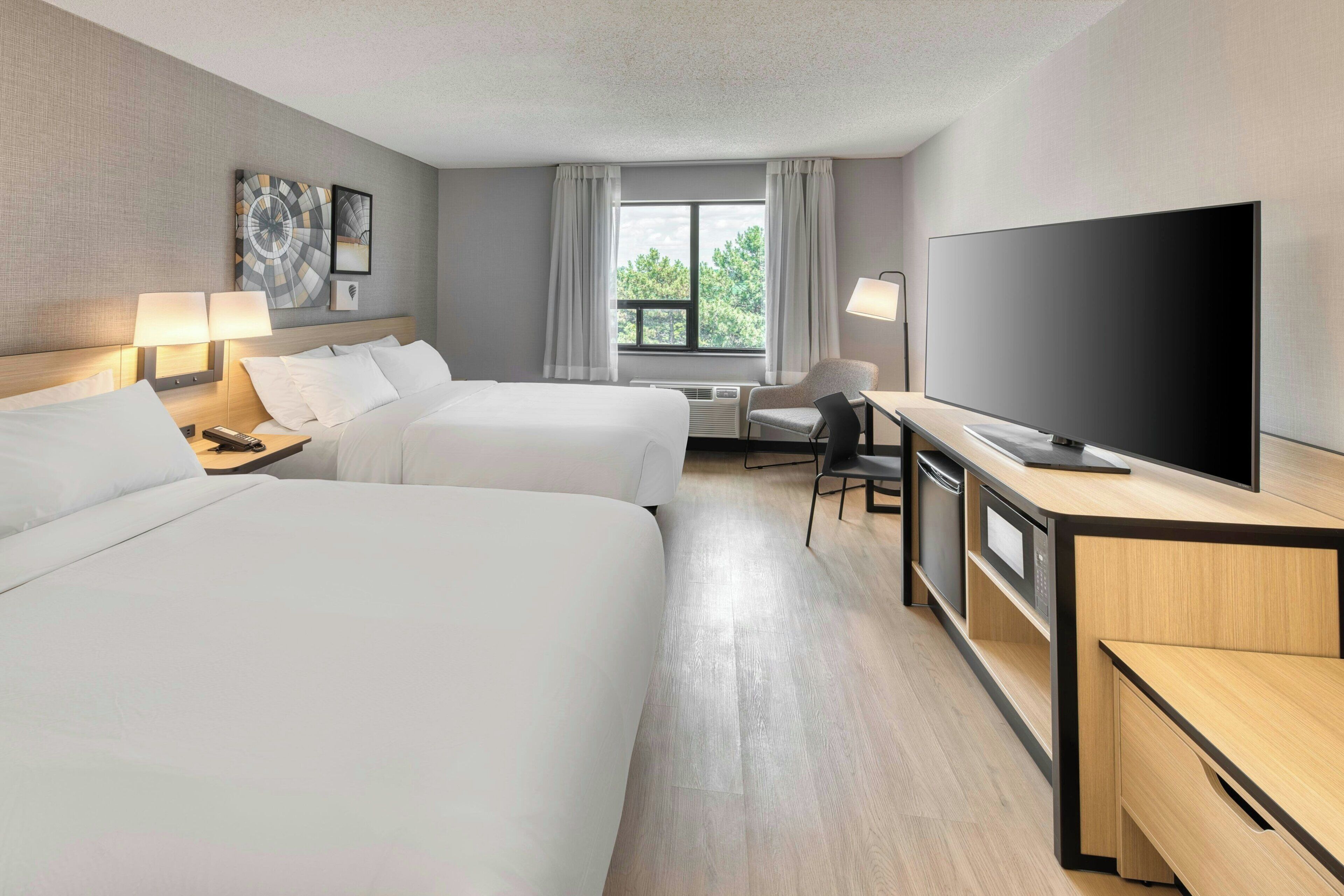 A hotel room with two beds, a TV, a desk, and a chair.