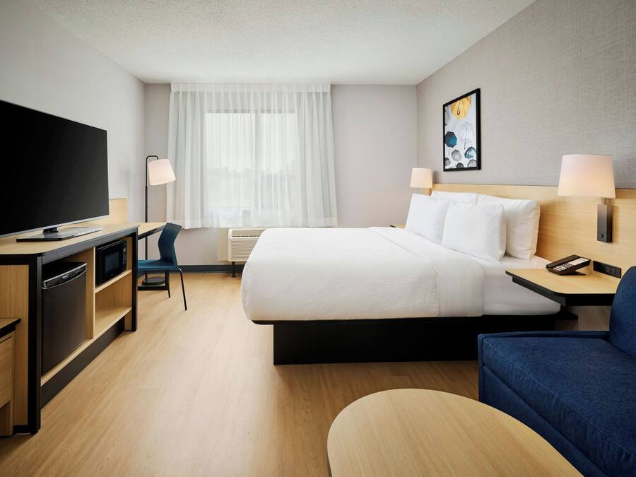 Ein Hotelzimmer mit Bett, Schreibtisch, Fernseher, Stuhl und einem Bild an der Wand.