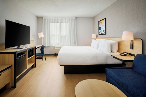 A hotel room with a bed, desk, television, chair, and a painting on the wall.