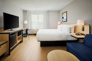 Habitación de hotel con cama, escritorio, televisor, silla y un cuadro en la pared.