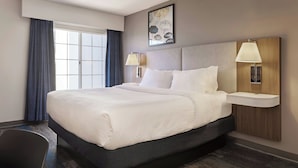 A hotel room with a large bed, two bedside lamps, a nightstand, a window with curtains, and a wall-mounted artwork. - City Express by Marriott Port Hope Cobourg (Port Hope)