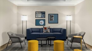 A modern hotel room with a blue sofa, two armchairs, a small coffee table, two floor lamps, and artwork on the wall. - City Express by Marriott Port Hope Cobourg (Port Hope)